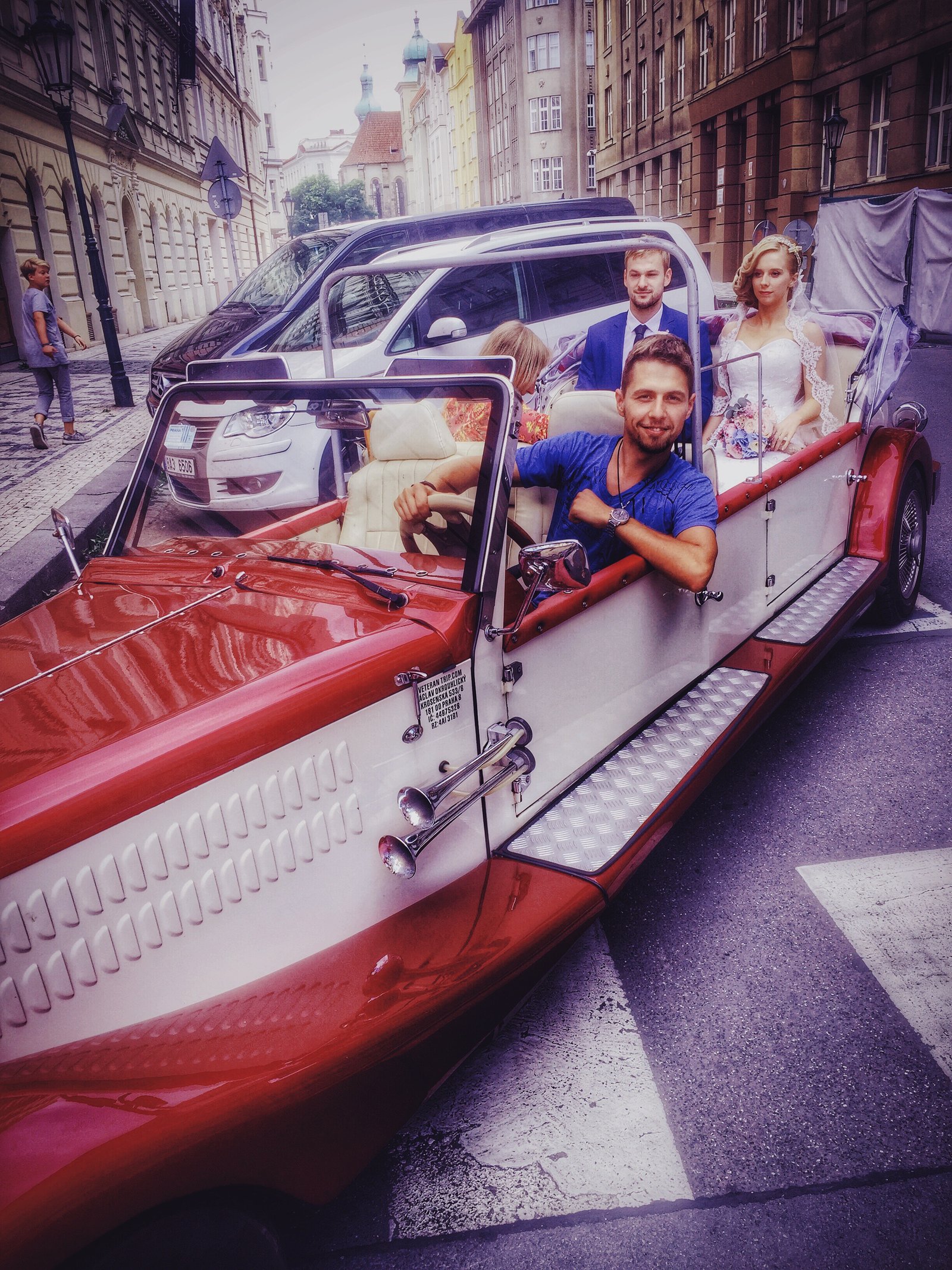 A couple riding through Prague in a vintage wedding car