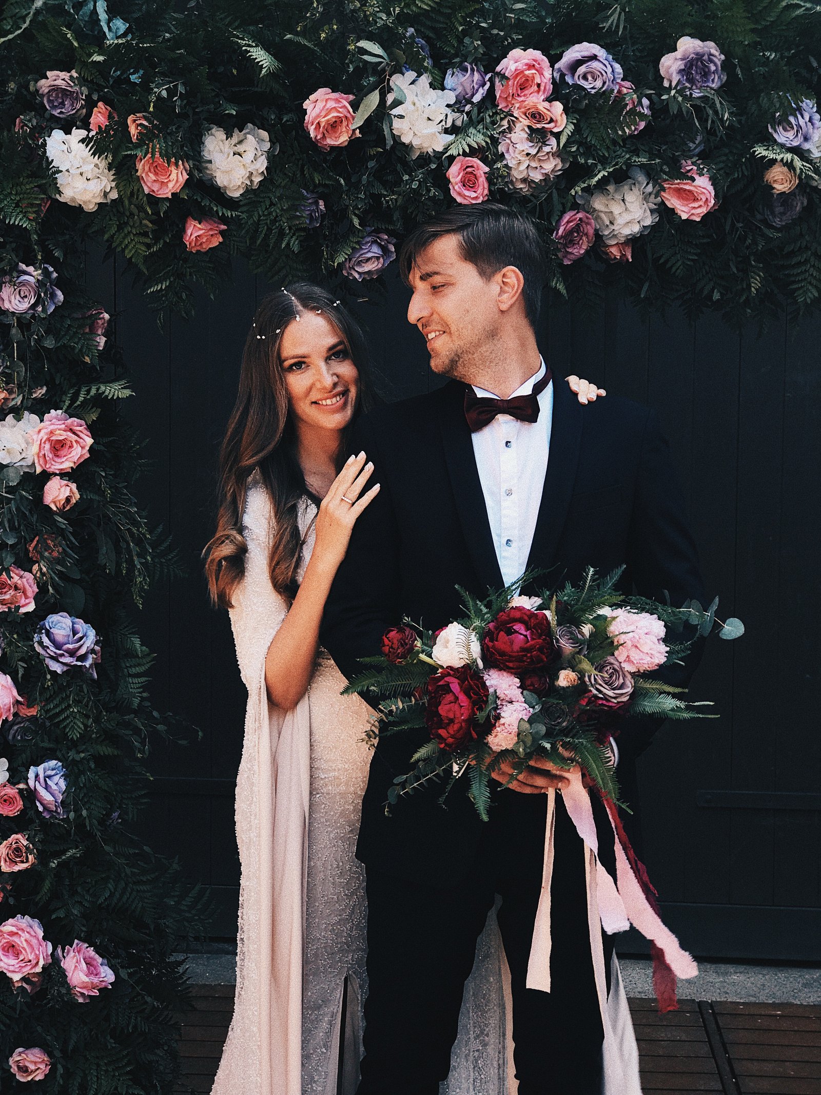 A newlywed couple standing together beneath a floral arch